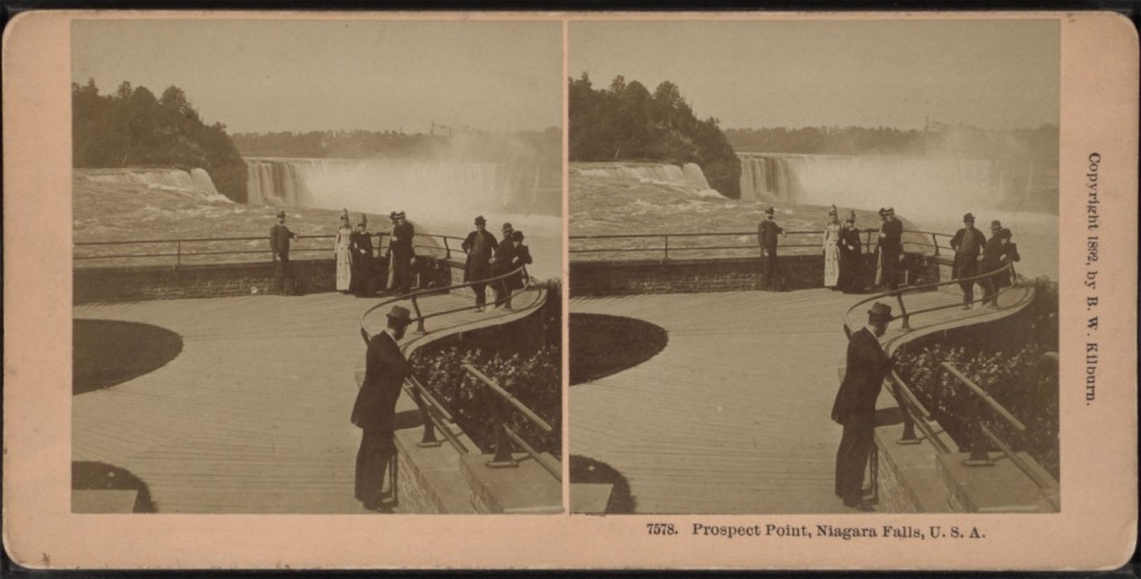A stereographic photograph taken at the Prospect Point observation area of Niagara Falls. There are multiple people who are standing in front of the falls, posing for the camera.